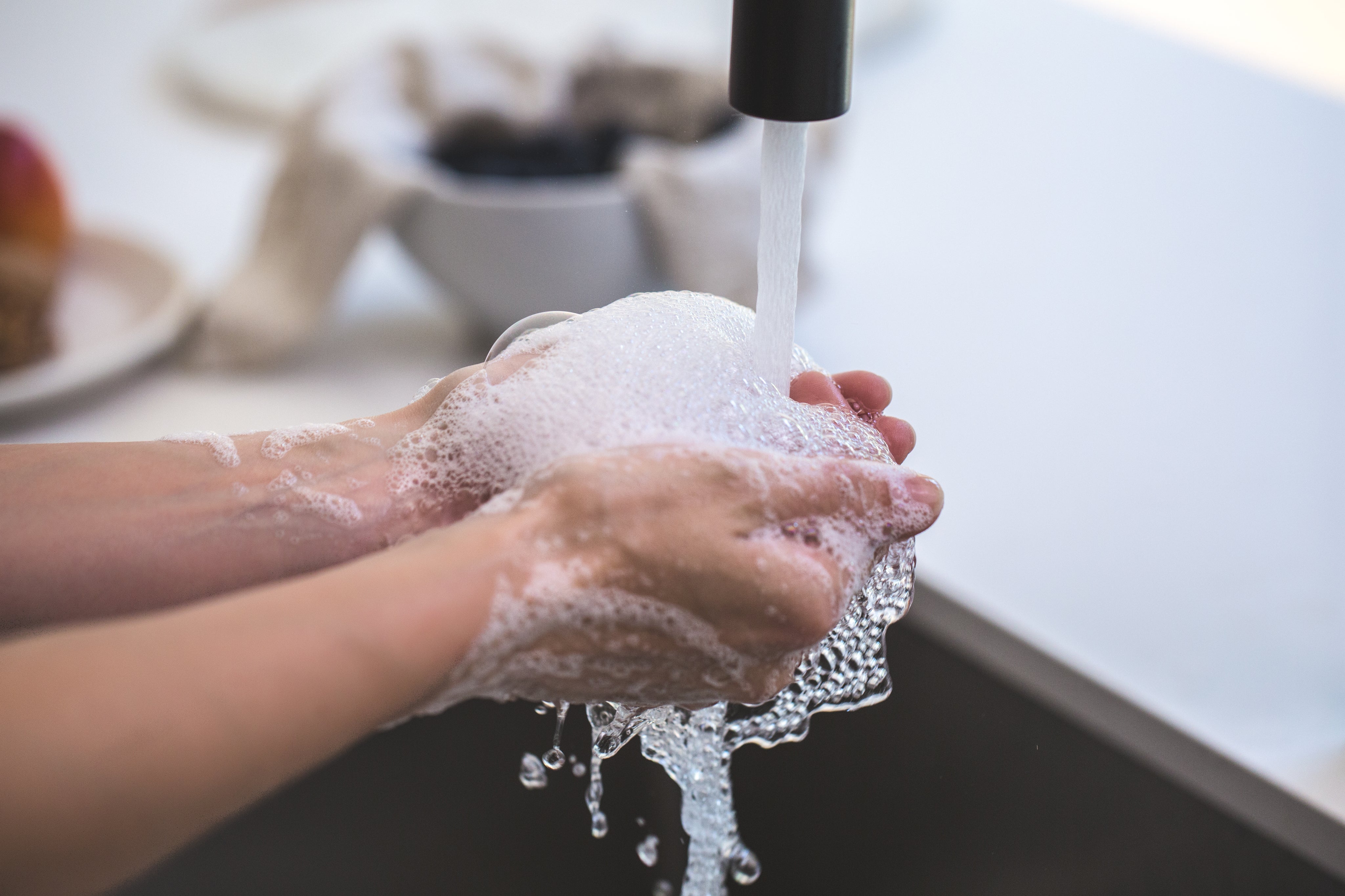 Washing soapy hands in a running faucet.